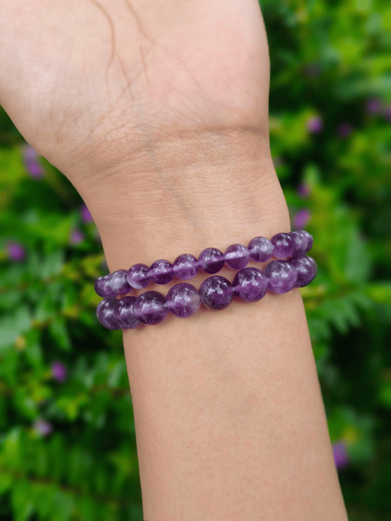 Amethyst round-bead bracelets worn together on a wrist outdoors.
