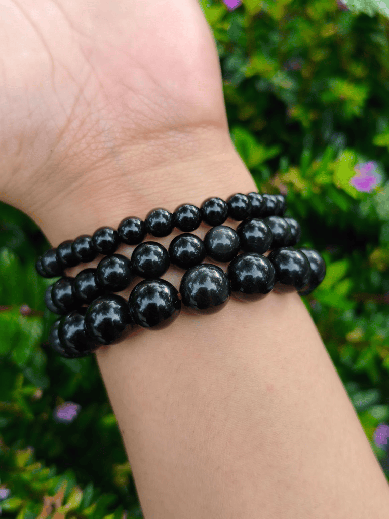 Black Obsidian round-bead bracelets worn together on a wrist outdoors.