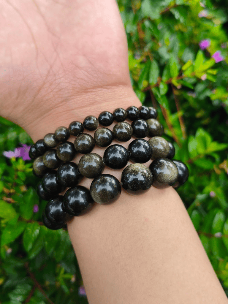 Golden Sheen Obsidian round-bead bracelets worn together on a wrist outdoors.