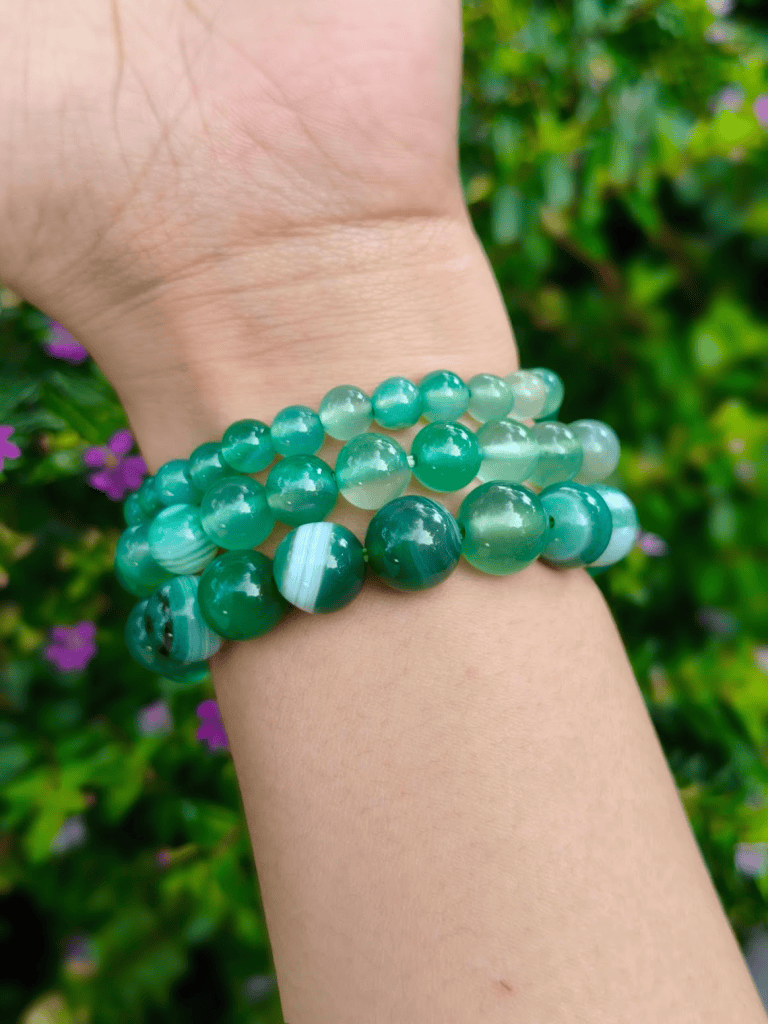Green Agate round-bead bracelets worn together on a wrist outdoors.