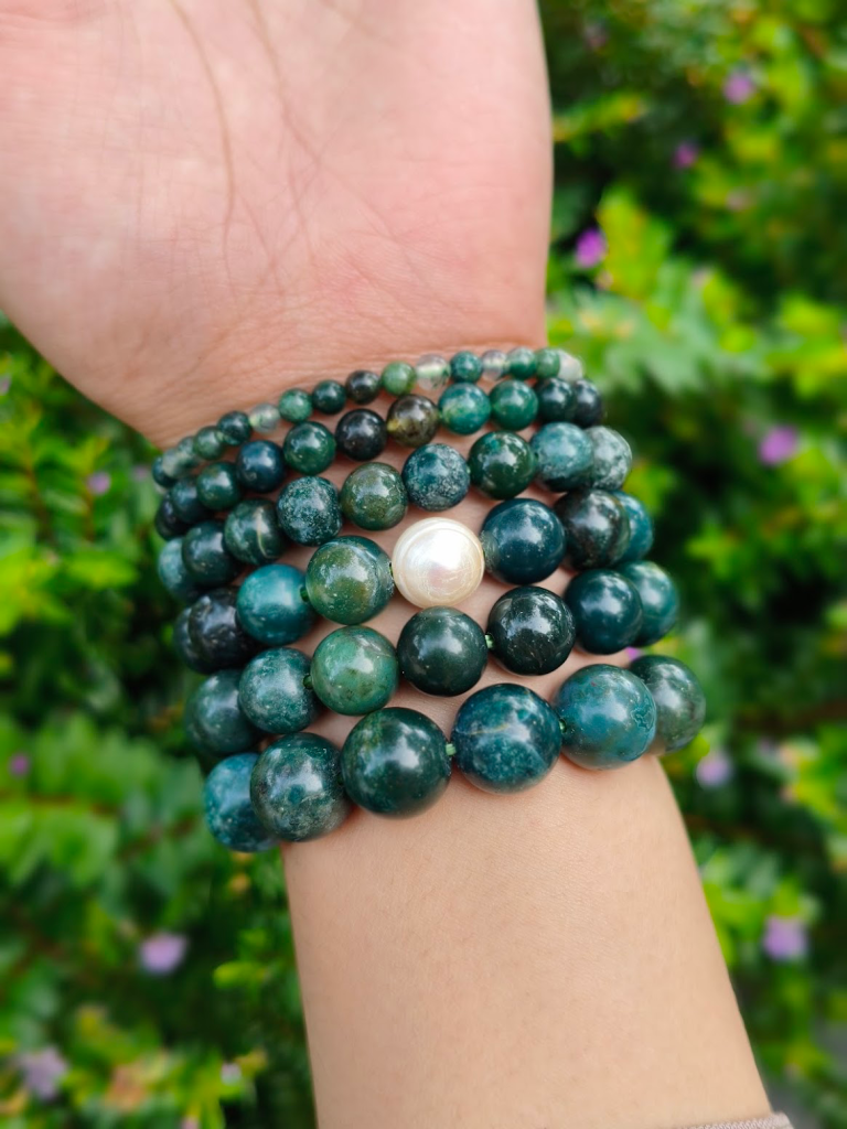 Moss Agate round-bead bracelets worn together on a wrist outdoors.