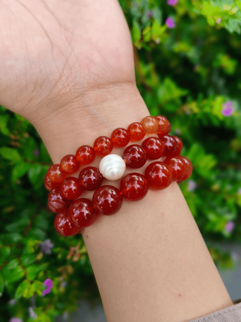 Red Agate round-bead bracelets worn together on a wrist outdoors.