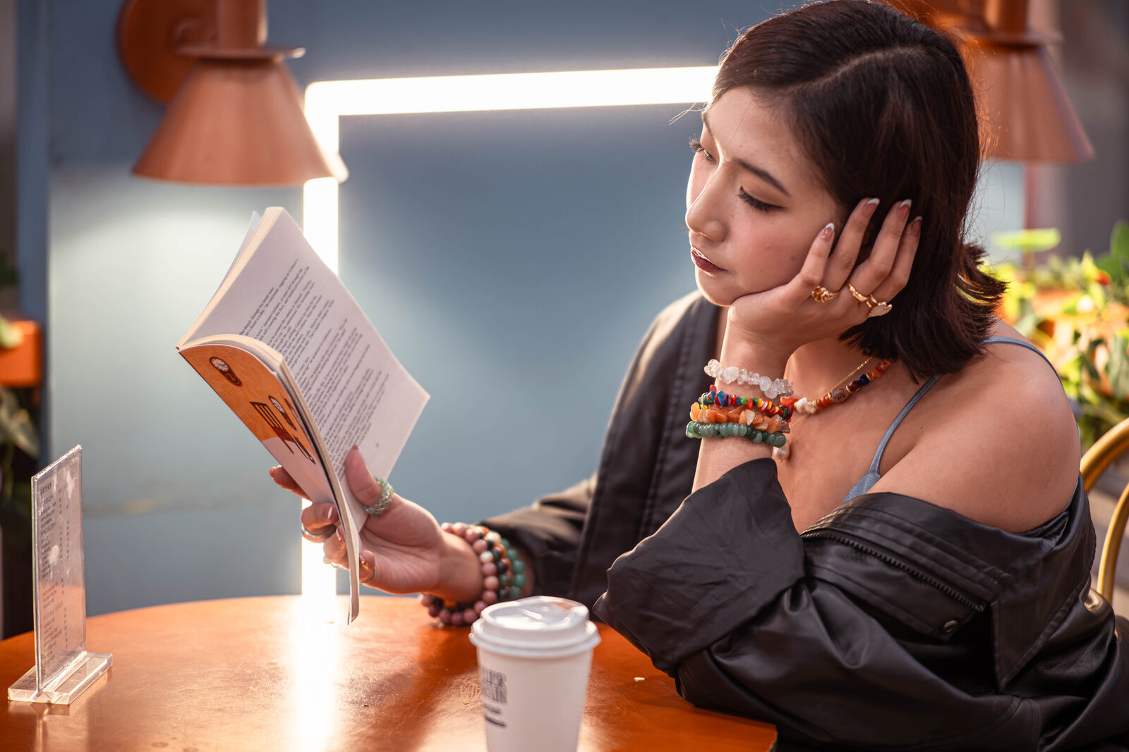 A TÁWID™ wearer reading while layered stone jewelry catches warm light.