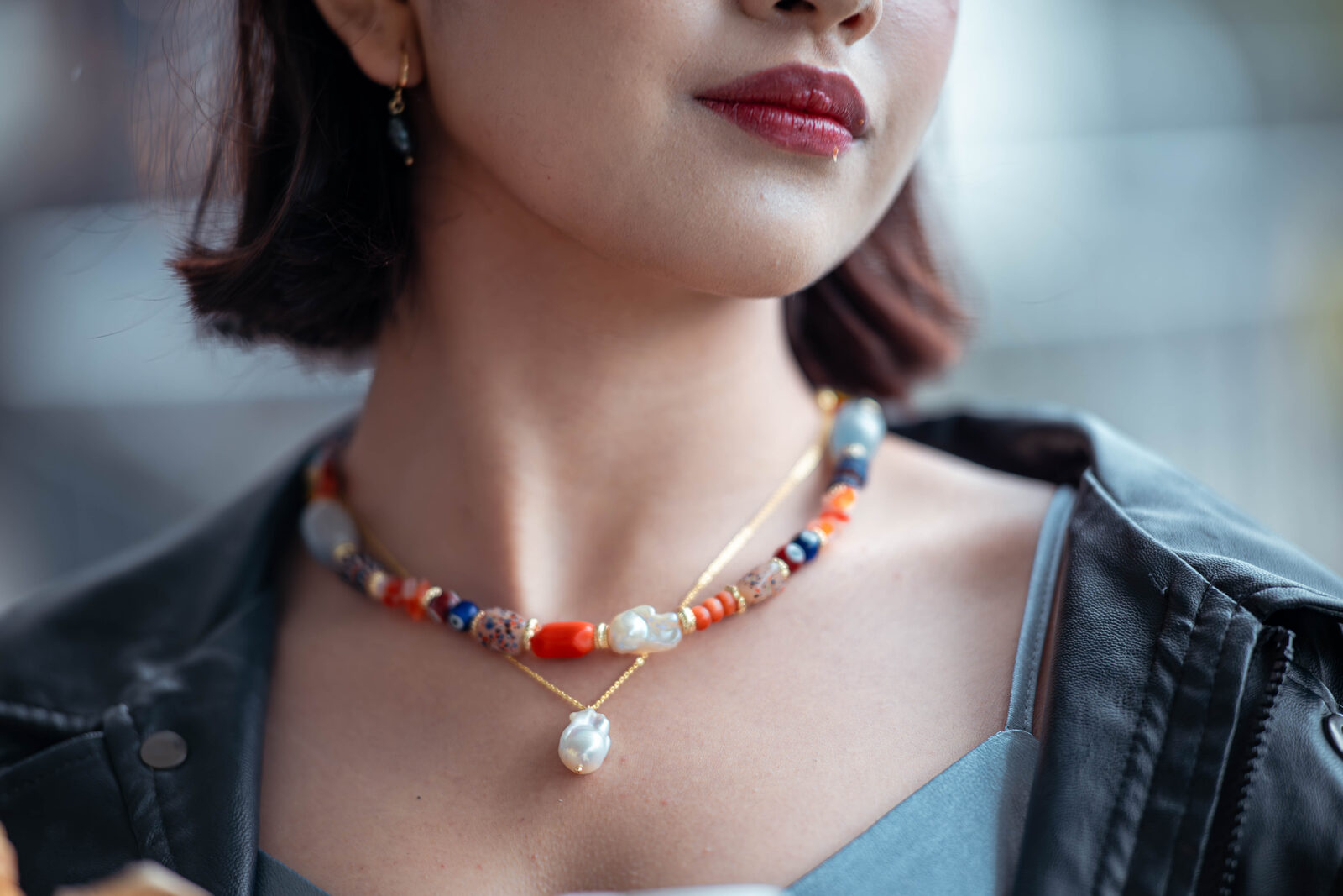 Close view of a TÁWID™ necklace combining coral-toned beads, pearl, and stone.